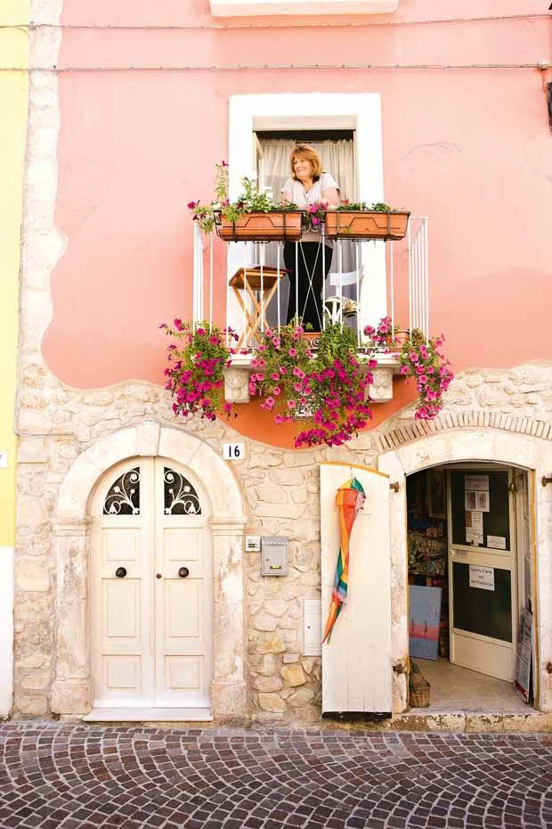 The flower-clad balcony off the bedroom is a place to watch the tapestry of life unfold in the Italian village where she lives for months each year.