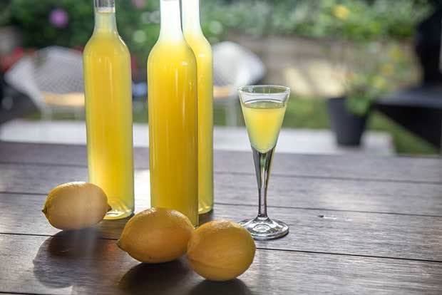 Three bottles of homemade limoncello with lemons and cocktail glass. 