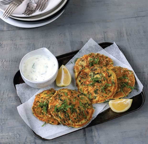 Savoury green pancakes on a plate with a side of yoghurt sauce and a lemon wedge. 