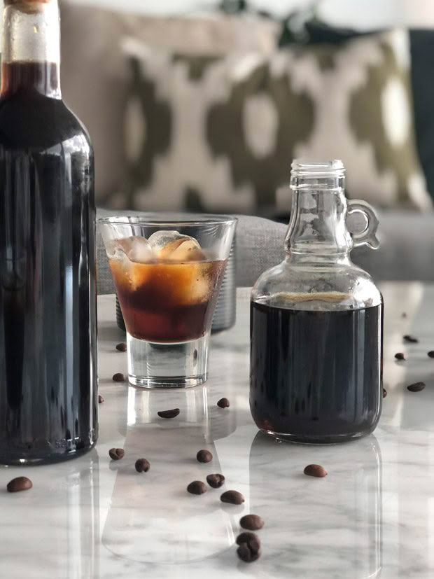 Bottles of homemade coffee liqueur with a shot glass of liqueur over ice.