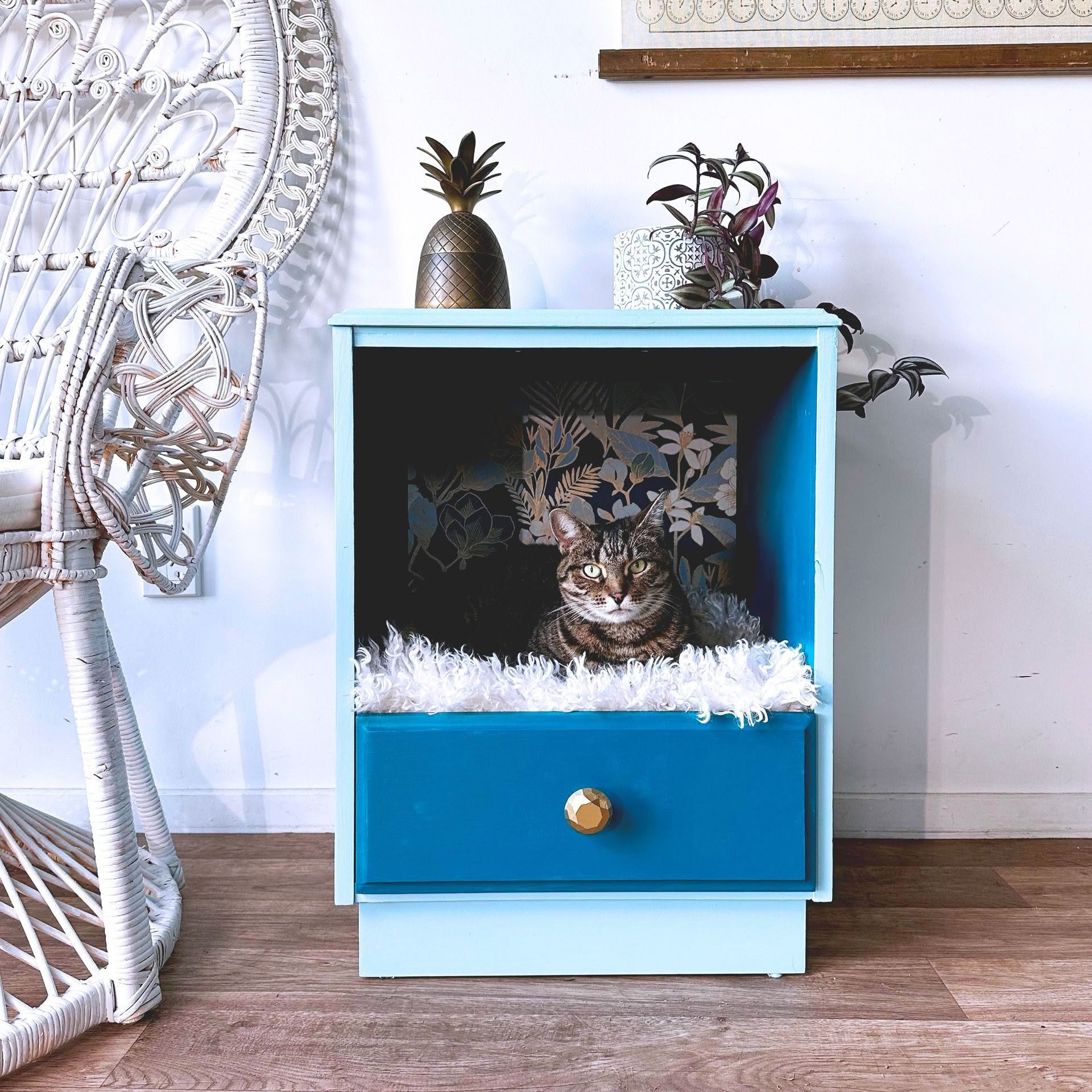 A cat is sitting in a blue drawer on a nightstand.