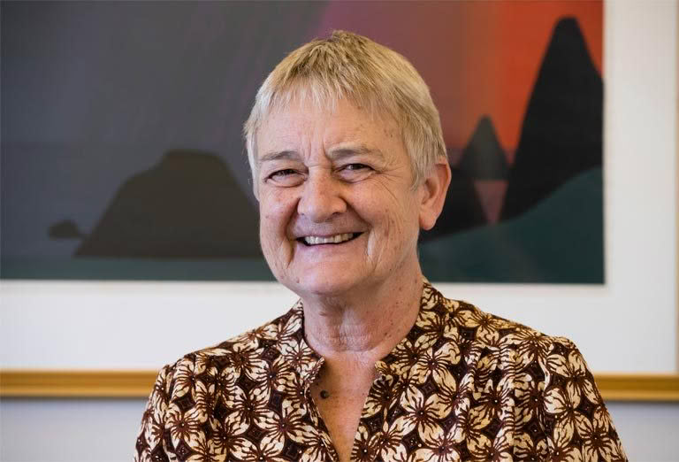 A woman in a floral shirt is smiling in front of a painting.