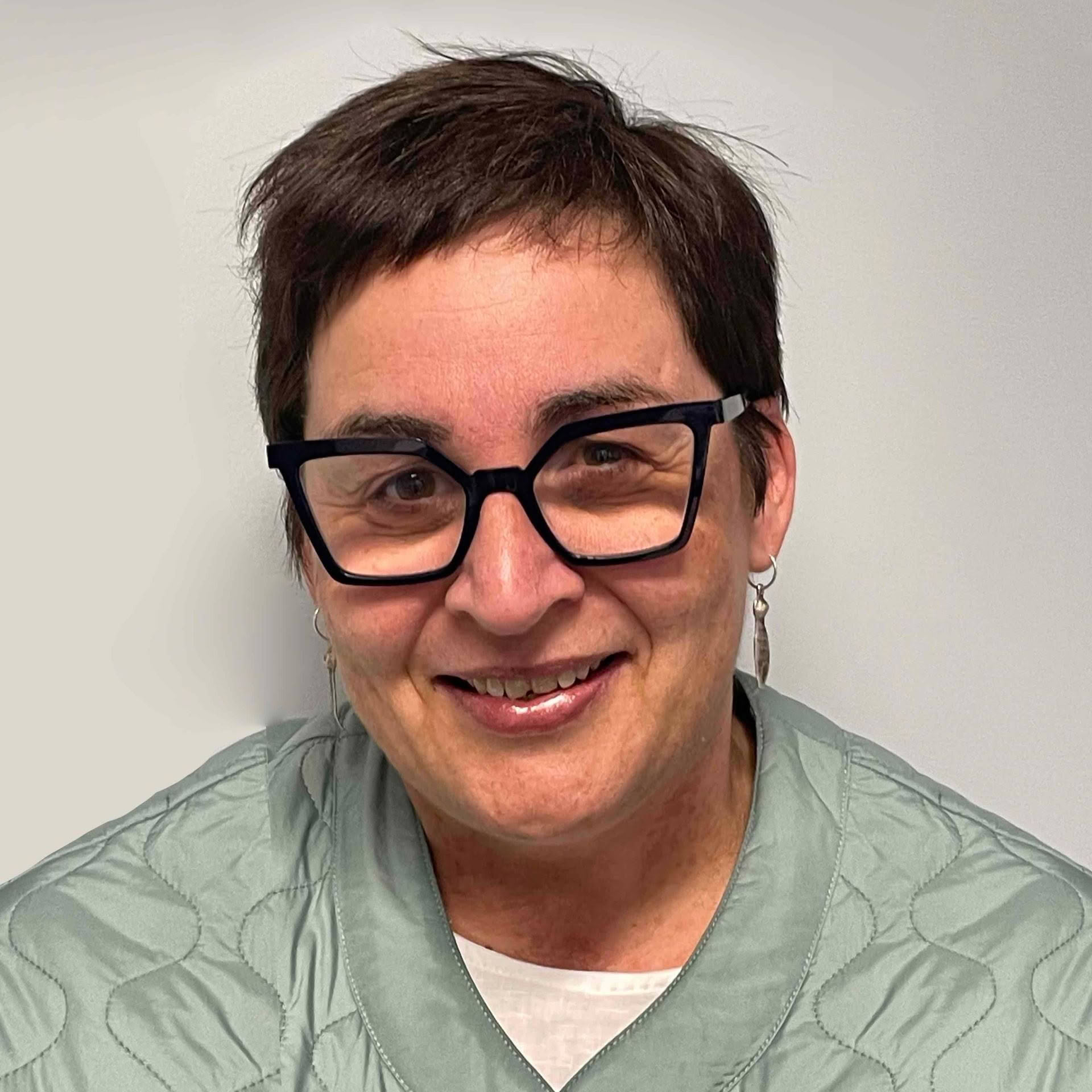 A woman wearing glasses and earrings is smiling for the camera.