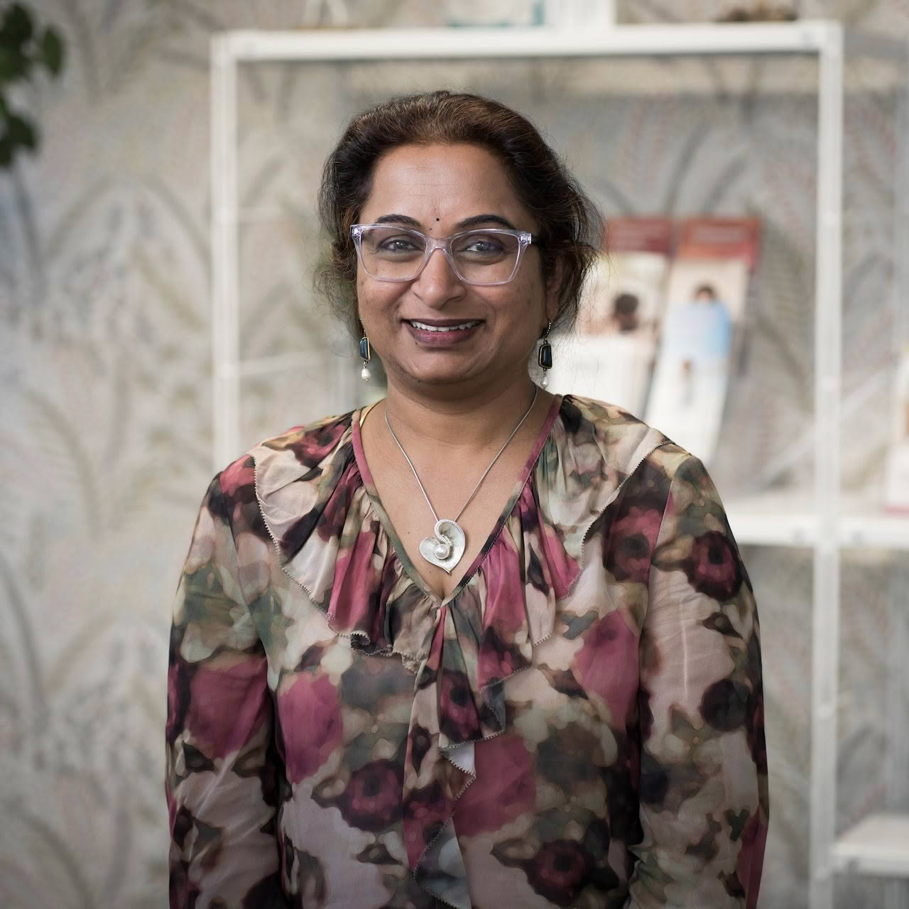 A woman wearing glasses and a floral shirt is smiling for the camera.