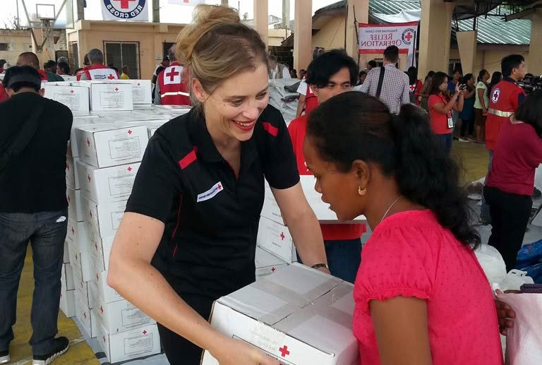 A woman in a red shirt is giving a box to another woman