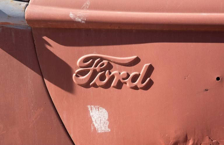 A close up of a ford logo on a rusty car door.