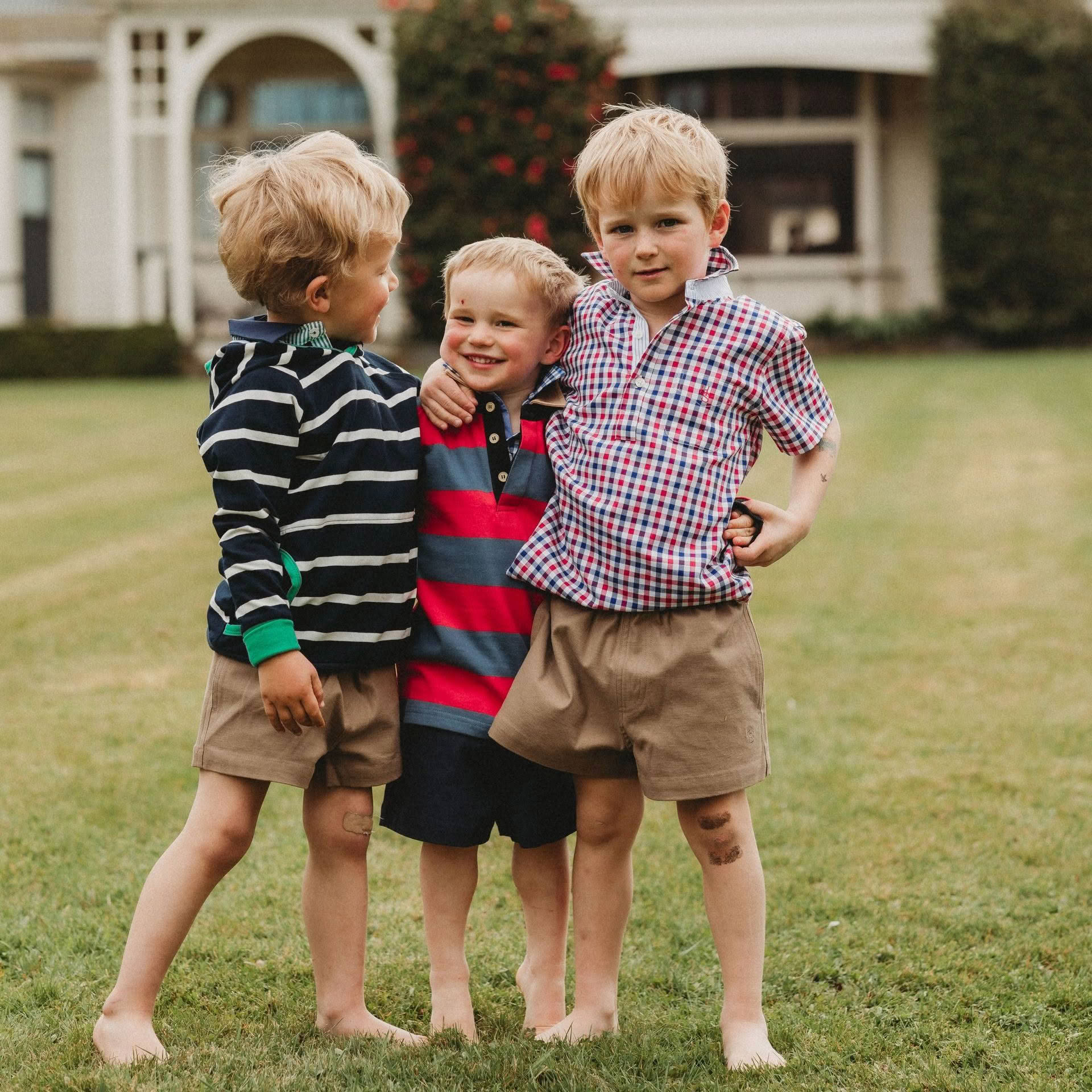 Three young boys are posing for a picture in front of a house