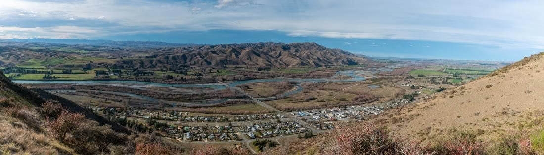 A panoramic view of a valley with mountains in the background and a river in the foreground.