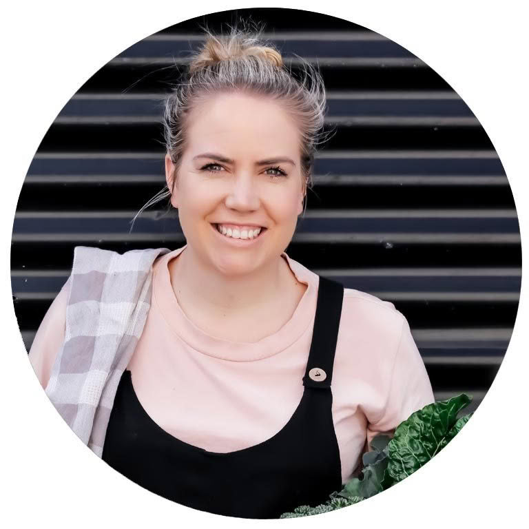 A woman in a pink shirt and black overalls is smiling