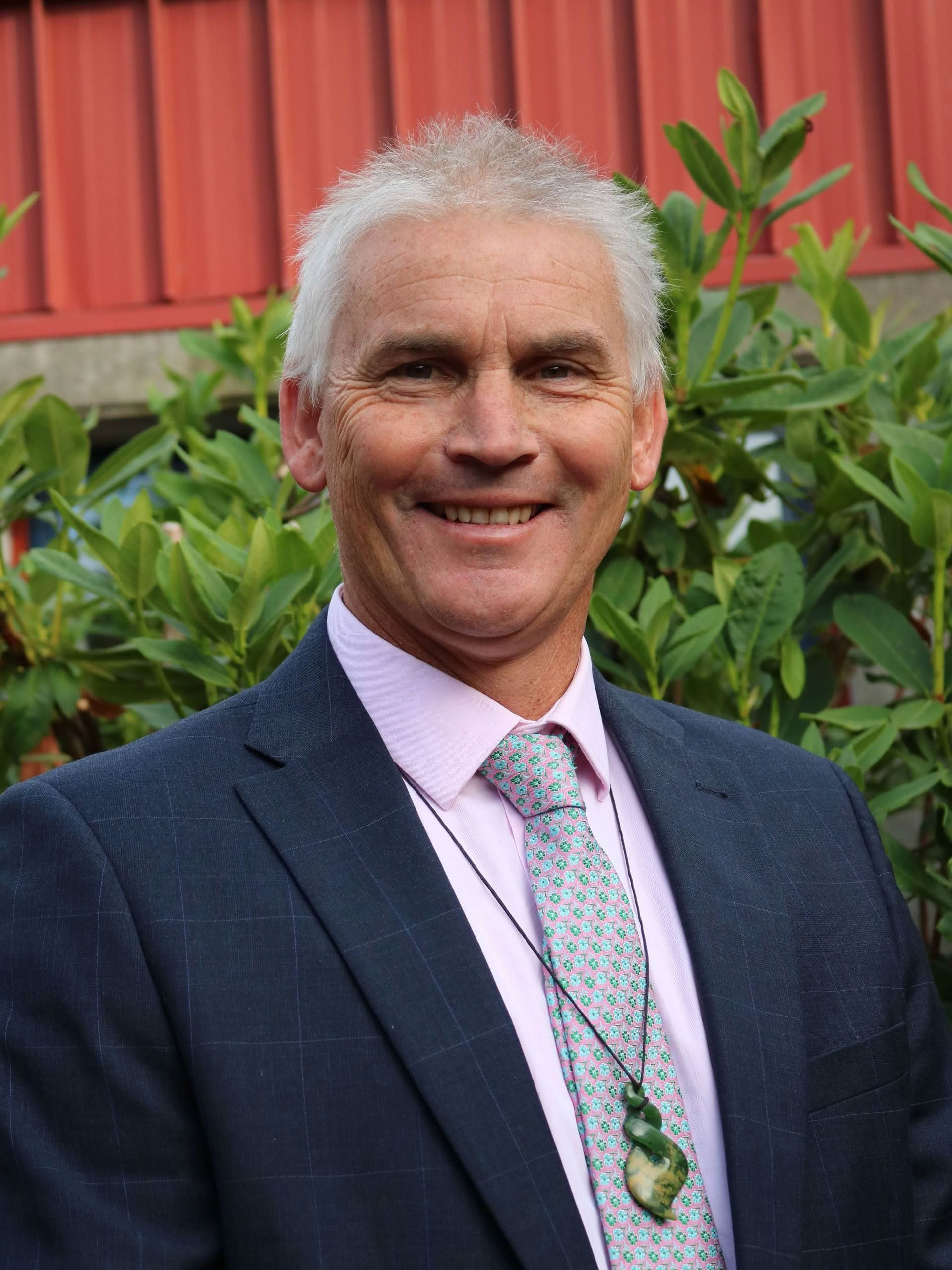 A man in a suit and tie is smiling in front of a red building.