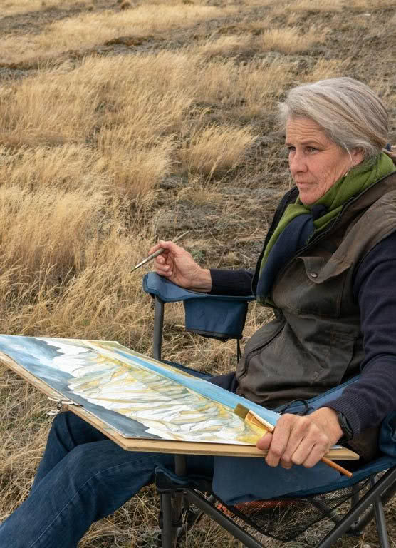 A woman is sitting in a chair painting a picture of a field.