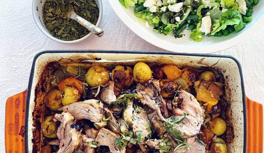 A casserole dish filled with meat and potatoes next to a bowl of salad.