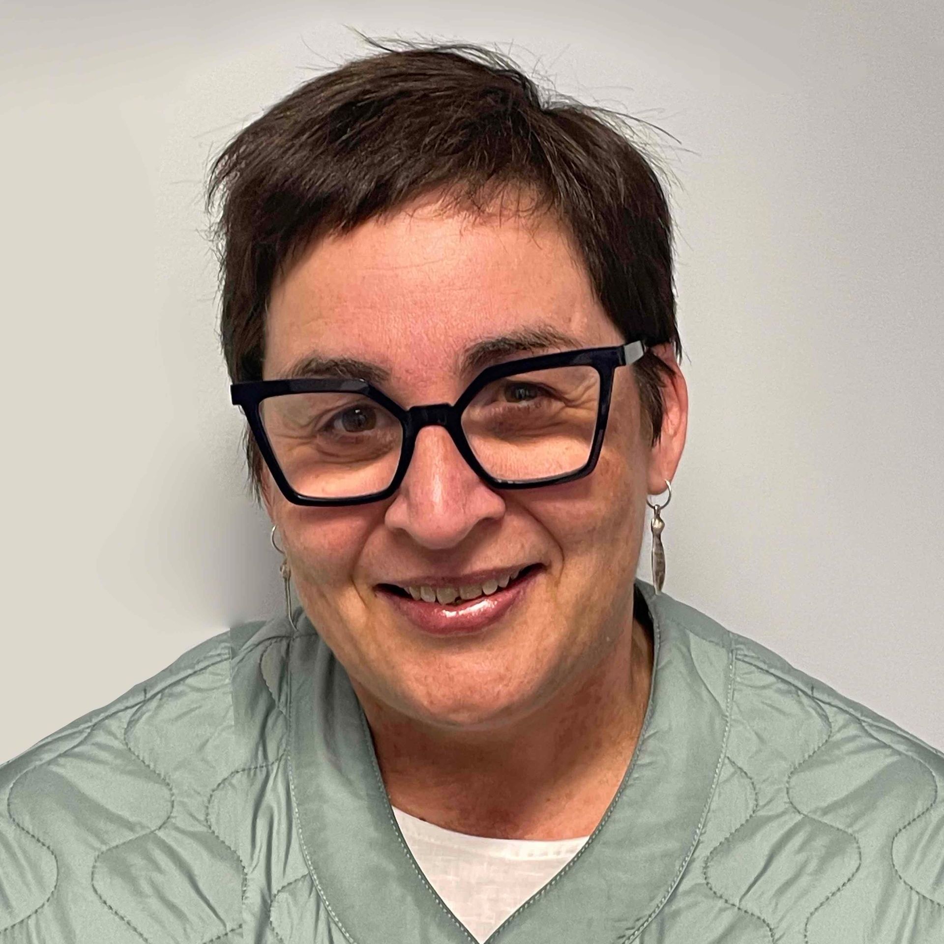 A woman wearing glasses and earrings is smiling for the camera.