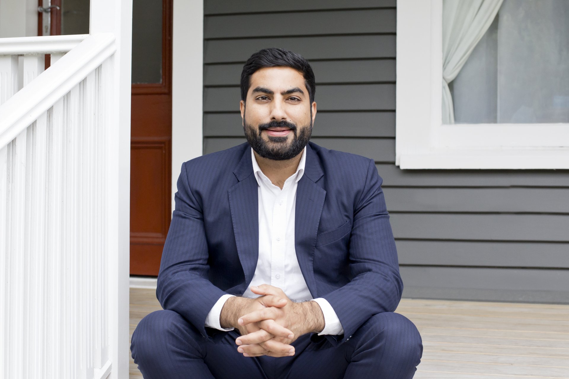 A man in a suit is sitting on the porch of a house.