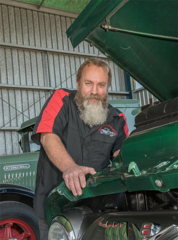 A man with a beard is looking under the hood of a green truck