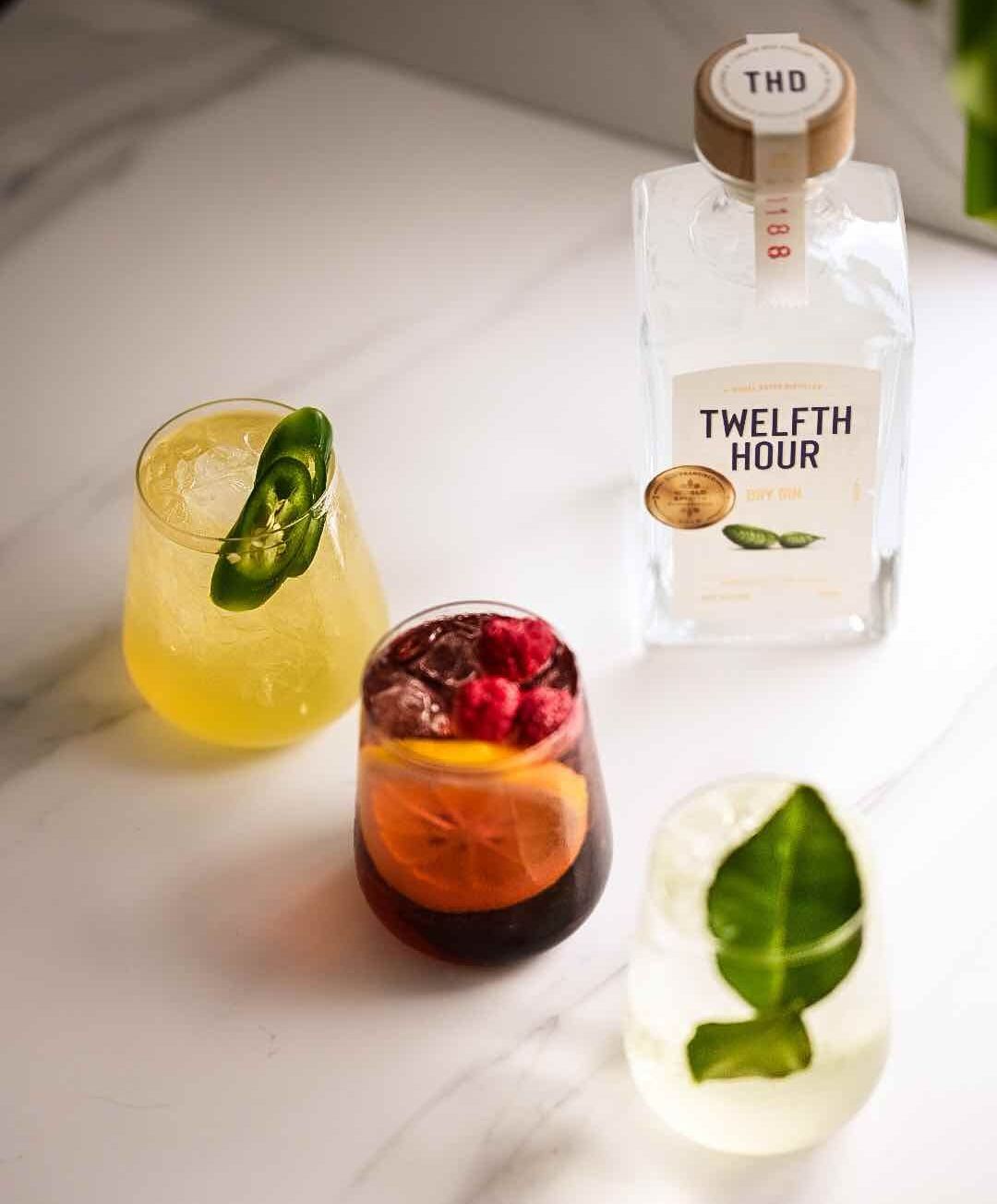 A bottle of twelfth hour is sitting on a table next to three glasses of drinks.