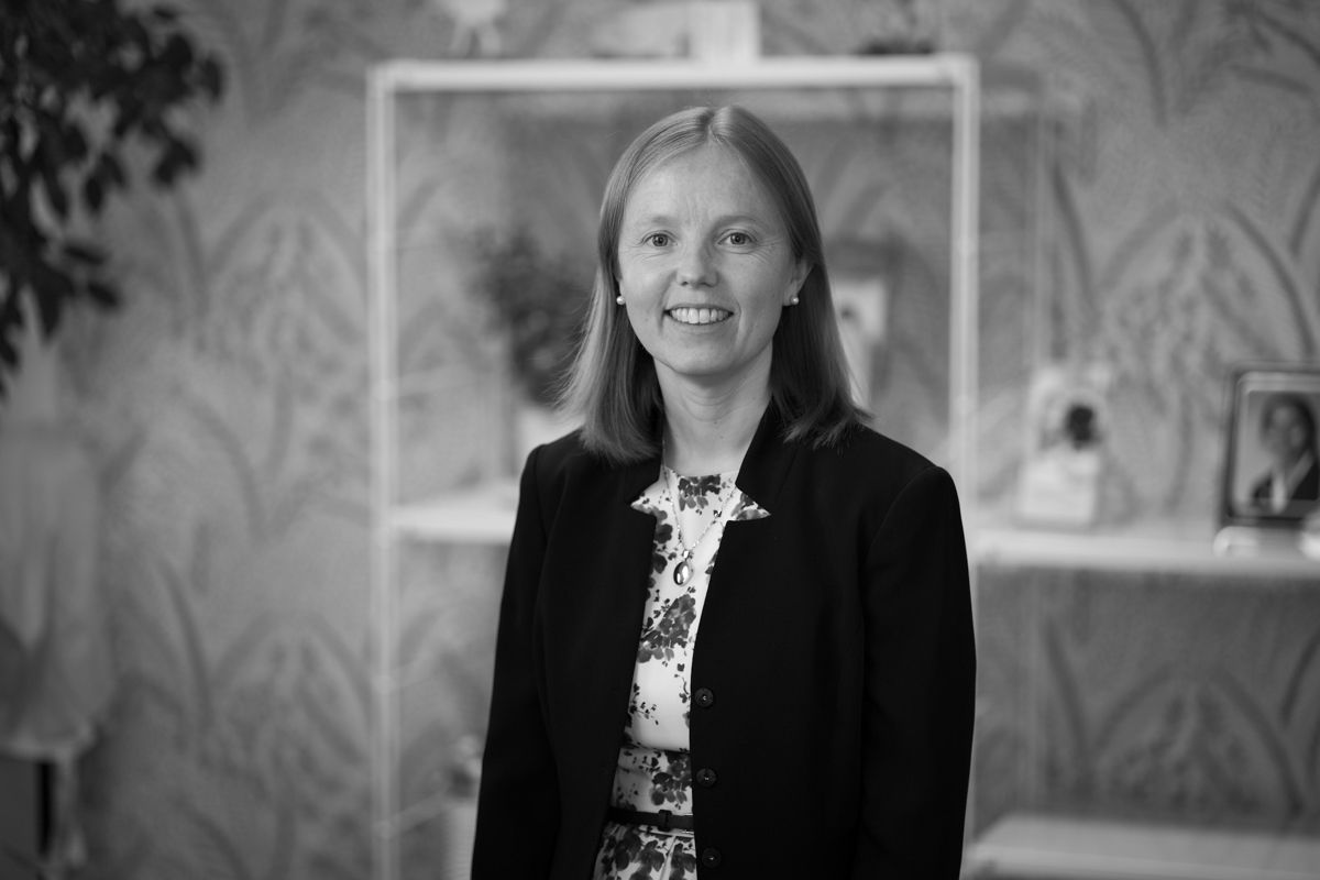 A black and white photo of a woman in a suit standing in front of a bookshelf.