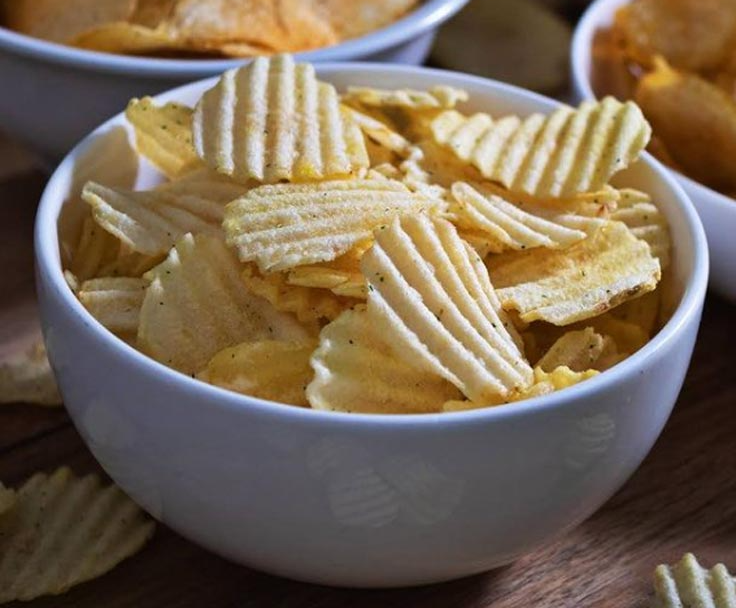 A bowl of potato chips is sitting on a wooden table.