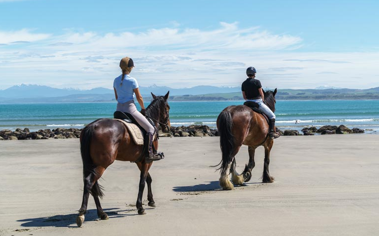Two people are riding horses on the beach.