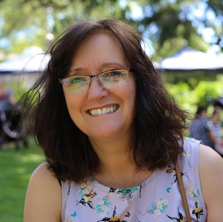 A woman wearing glasses and a floral shirt is smiling for the camera.