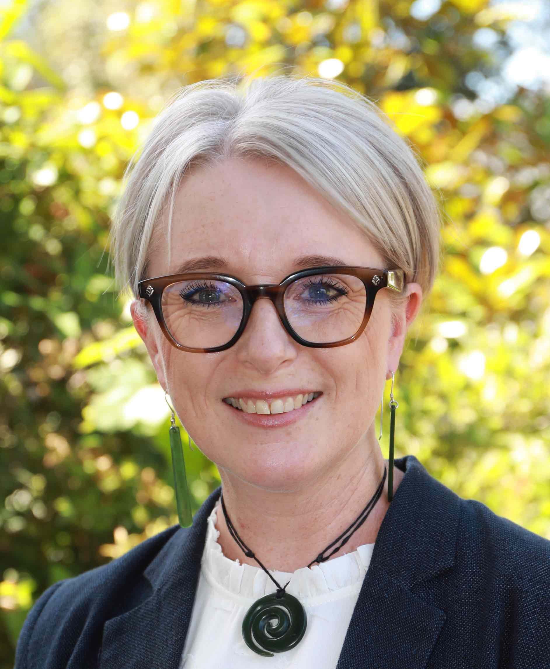A woman wearing glasses and a necklace is smiling for the camera.