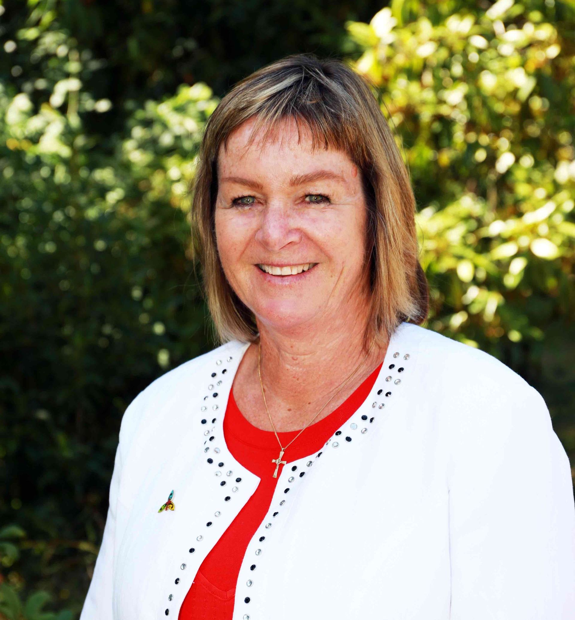 A woman wearing a white jacket and a red shirt is smiling for the camera.