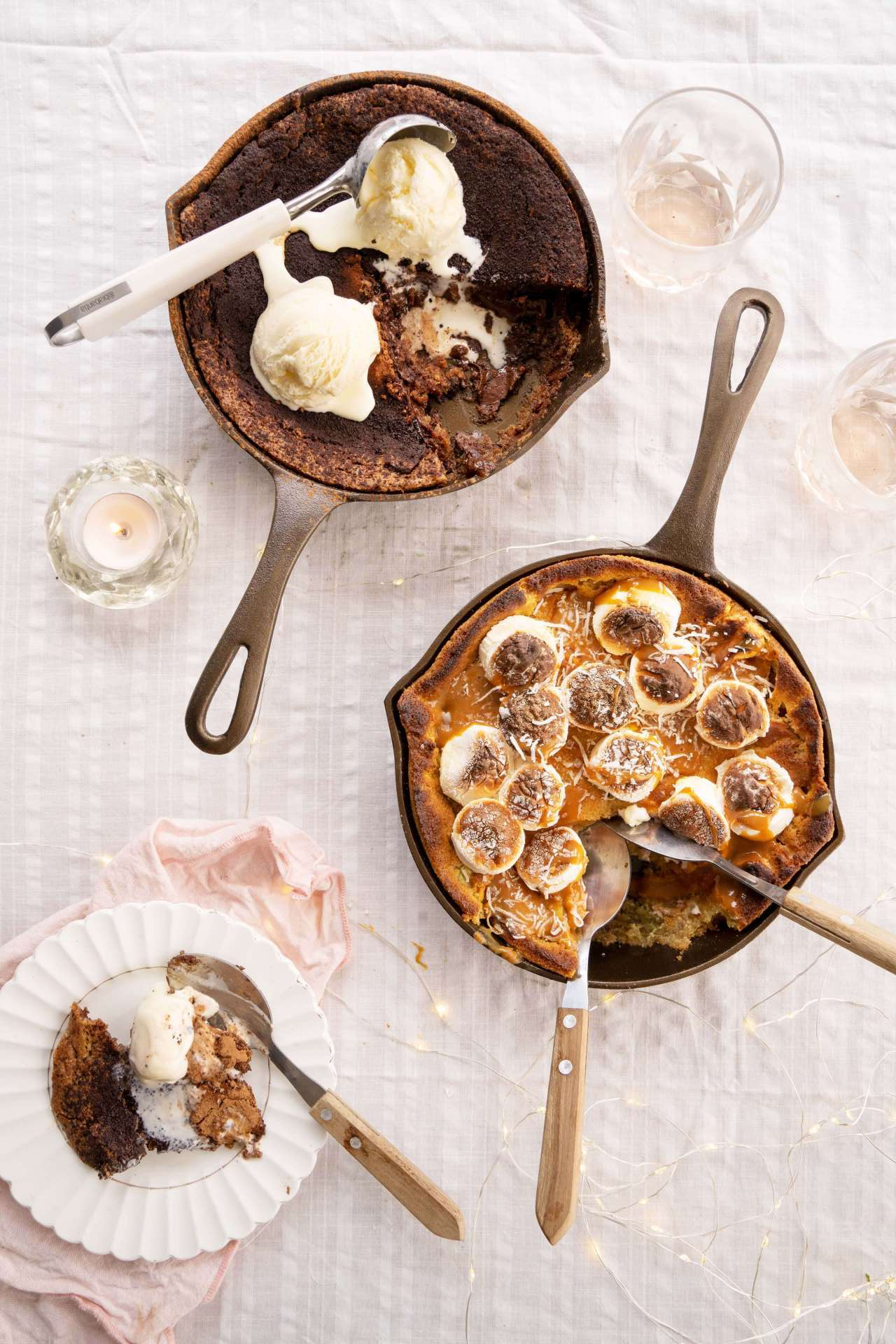 Two skillets of food with ice cream and spoons on a table.