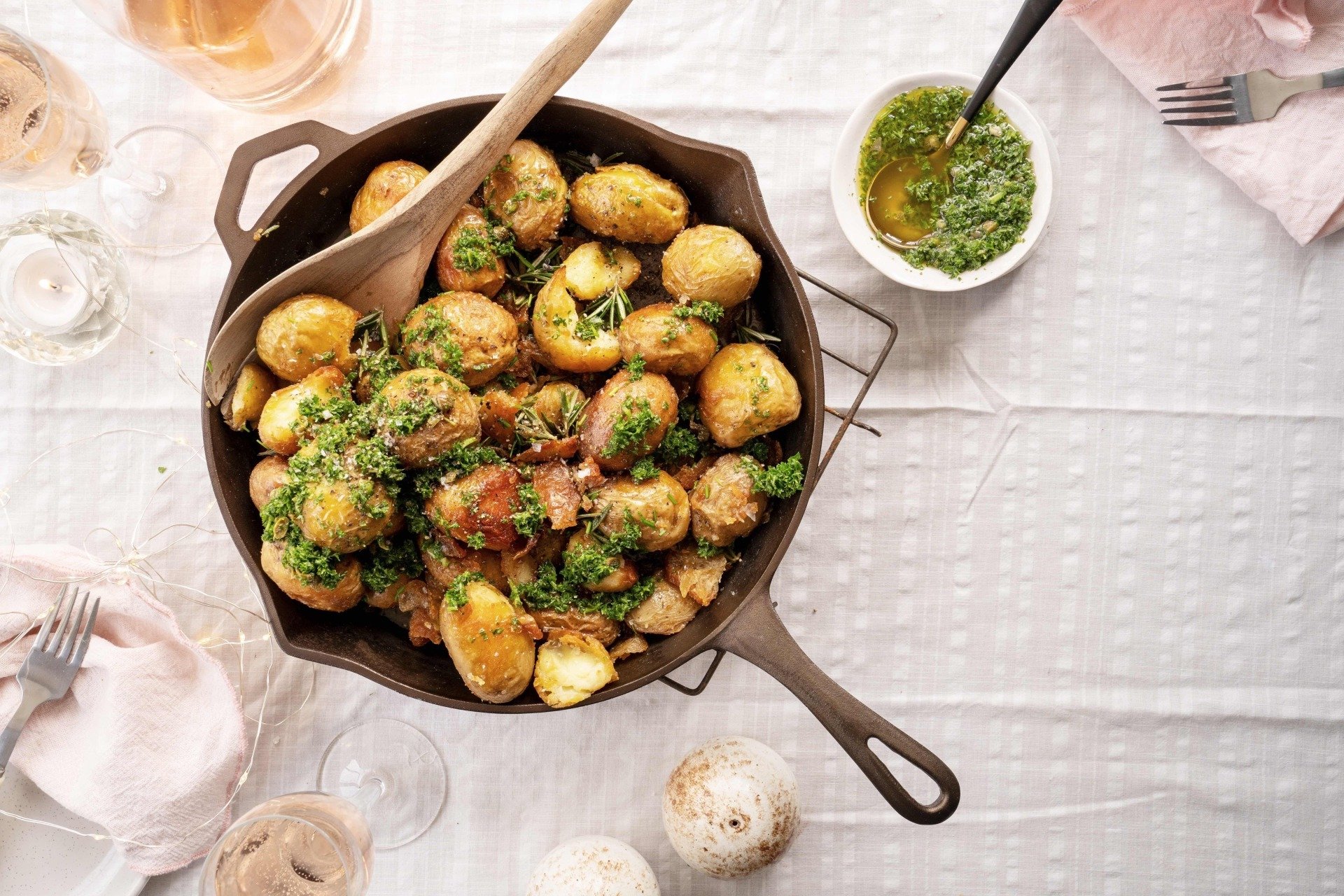A skillet filled with potatoes and a wooden spoon on a table.