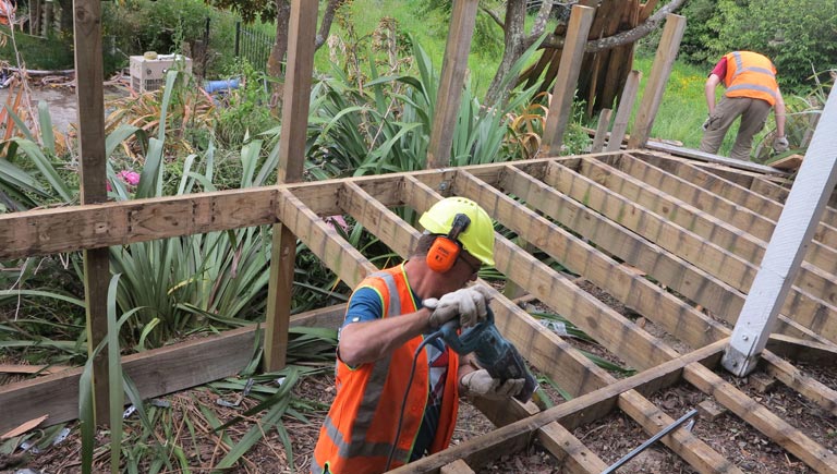 A man is using a drill on a wooden deck.