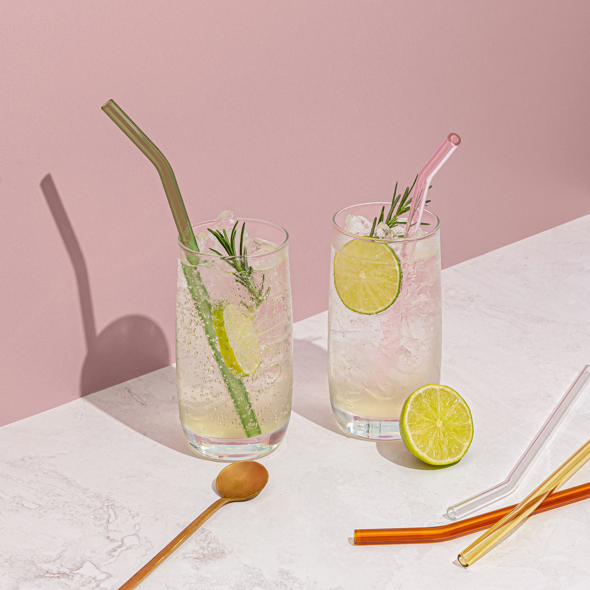 Two glasses of drinks with straws and a spoon on a table.