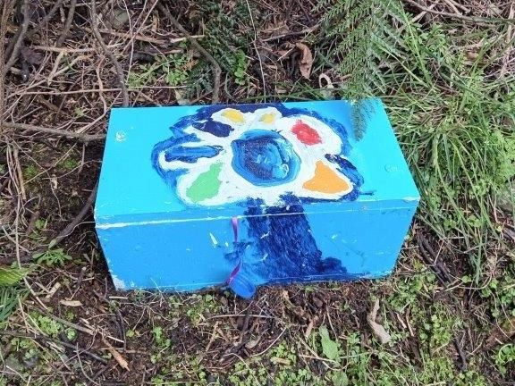 A blue box with a flower painted on it is sitting in the grass.